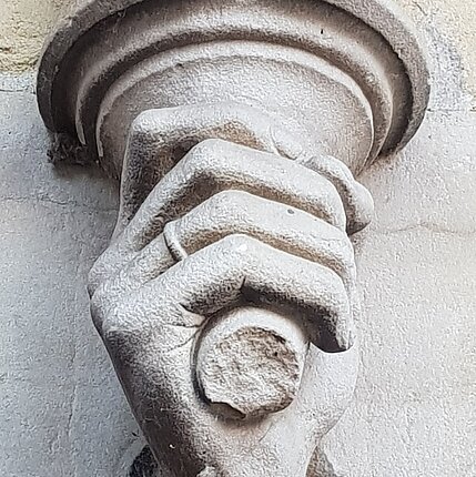 Eine Skulptur links von der Hochzeitspforte zeigt eine Hand mit Ehering, die die aufsteigende Säule wie eine Fackel umfasst